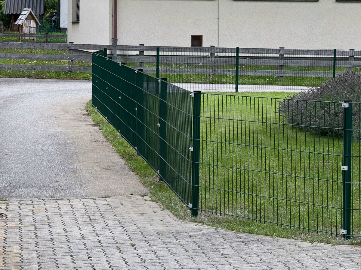 Grüner Doppelstabmattenzaun entlang einer gepflasterten Einfahrt